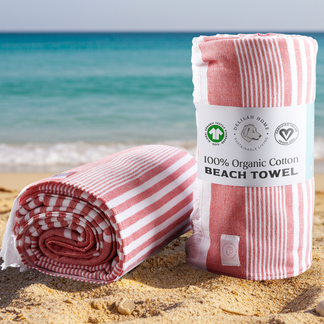 Two red striped 100% organic cotton beach towels rolled on the sand